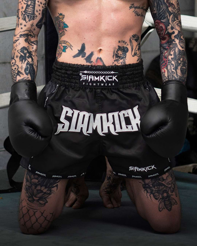 Fighter kneeling in black SIAMKICK Muay Thai shorts and gloves
